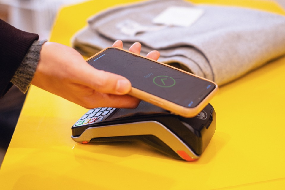 Hand h&auml;lt ein Smartphone an ein Kartenleseger&auml;t, auf dem Display erscheint die Best&auml;tigung der Zahlung